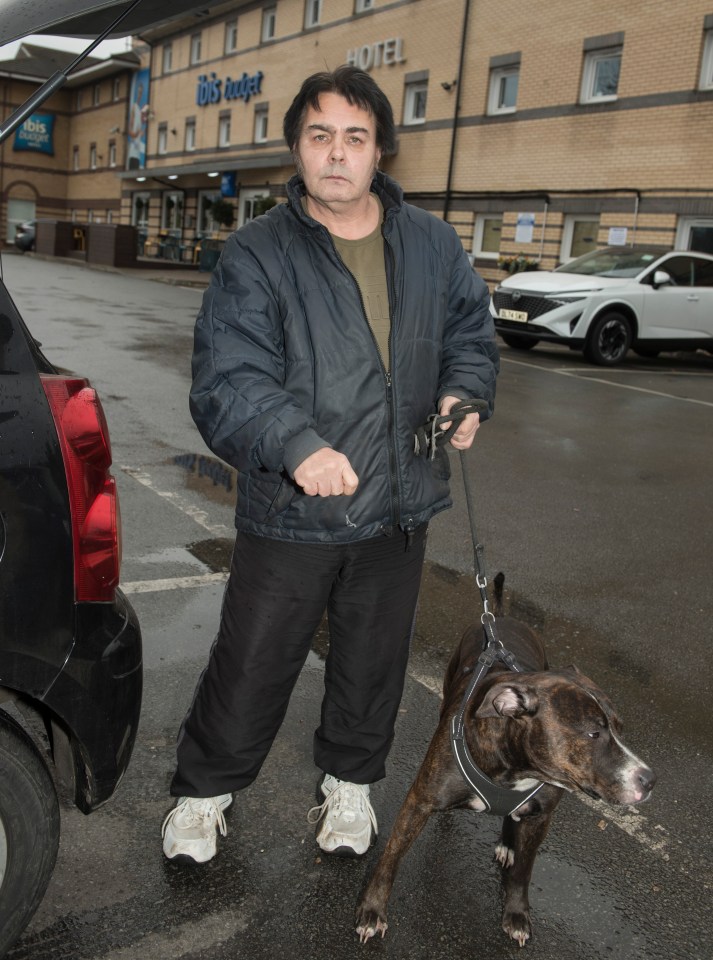 A homeless man with his dog standing in a parking lot.