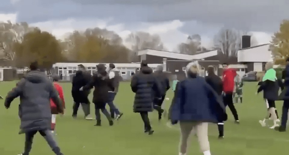 Adults running onto a soccer field during a children's game.