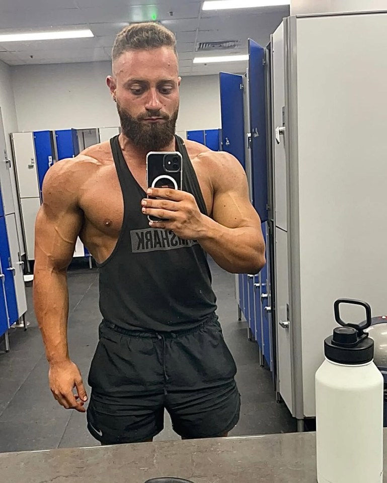 A muscular man taking a selfie in a gym locker room.