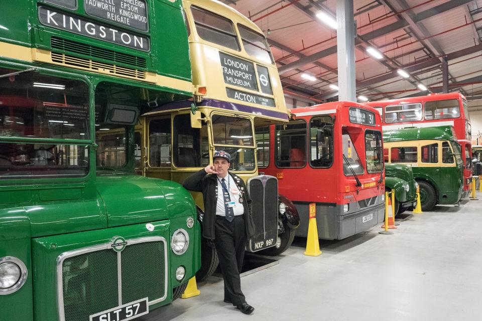 A man stands in front of vintage buses at the London Transport Museum.