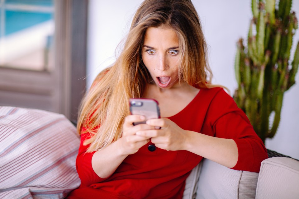 Woman in red dress looking shocked at her phone.