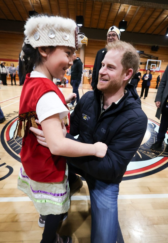 Prince Harry interacting with a young girl in traditional Indigenous clothing.