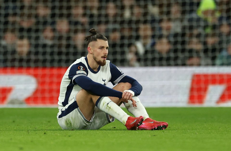 Radu Dragusin of Tottenham Hotspur sitting on the field looking dejected after an injury.