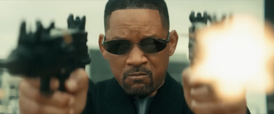 Will Smith in a music video still, aiming two guns.