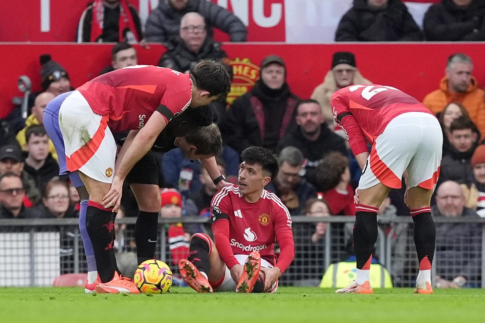 Lisandro Martinez of Manchester United on the ground injured, attended to by teammates.