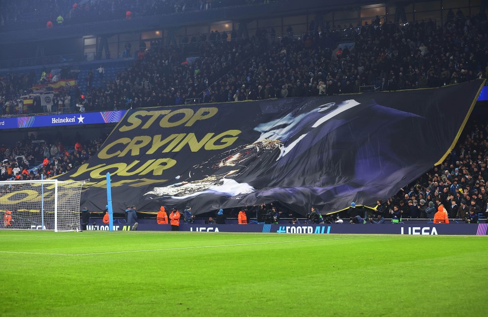 A large banner reading "Stop Crying Your Heart Out" is unfurled in a stadium.