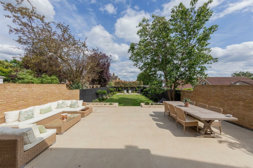 Backyard patio with seating area and dining table, overlooking a lawn and garden.