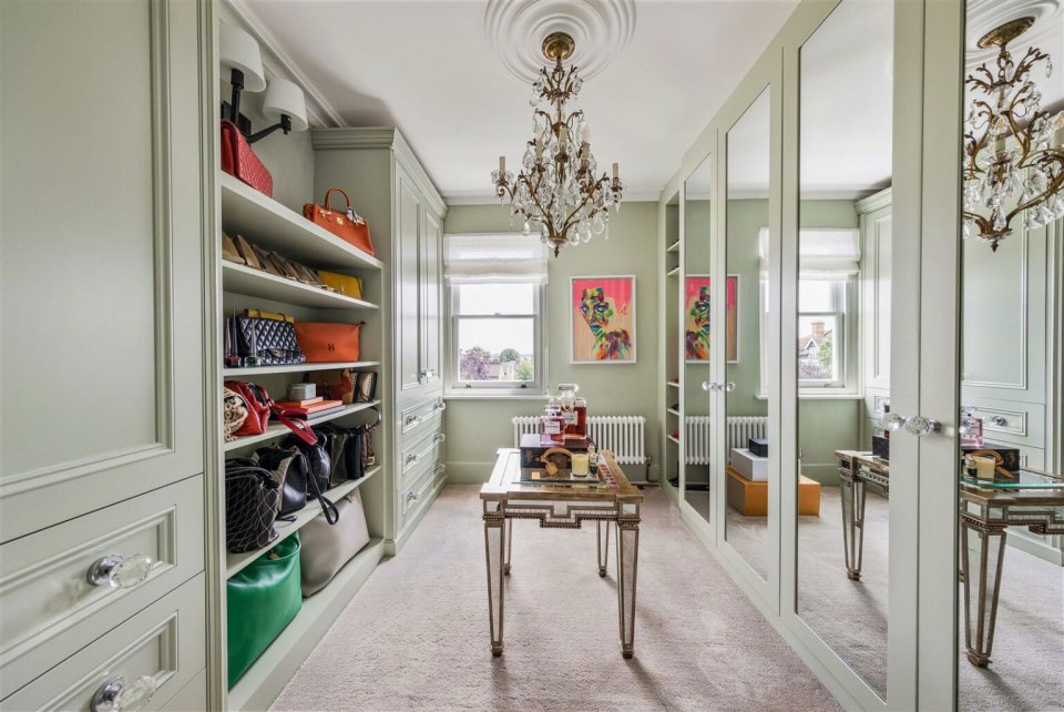 Interior view of a large walk-in closet with mirrored doors, shelves filled with handbags, and a mirrored coffee table.