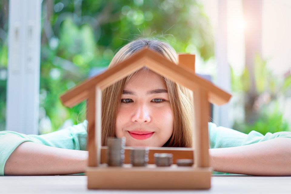 Woman looking at coins in a miniature house.