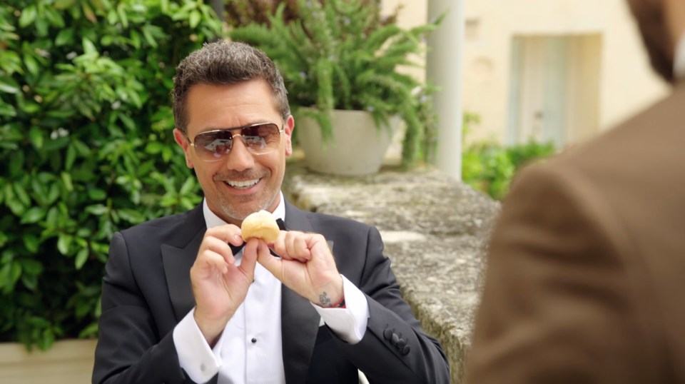 Man in tuxedo holding a small pastry.