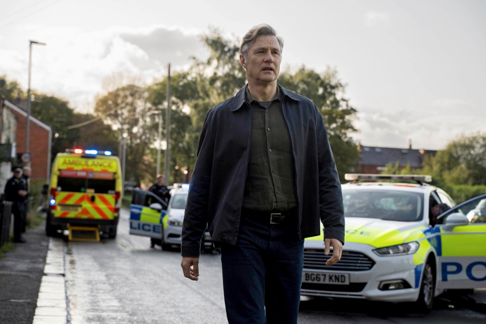 Ian St Clair (David Morrissey) walking past police cars and an ambulance in Sherwood.