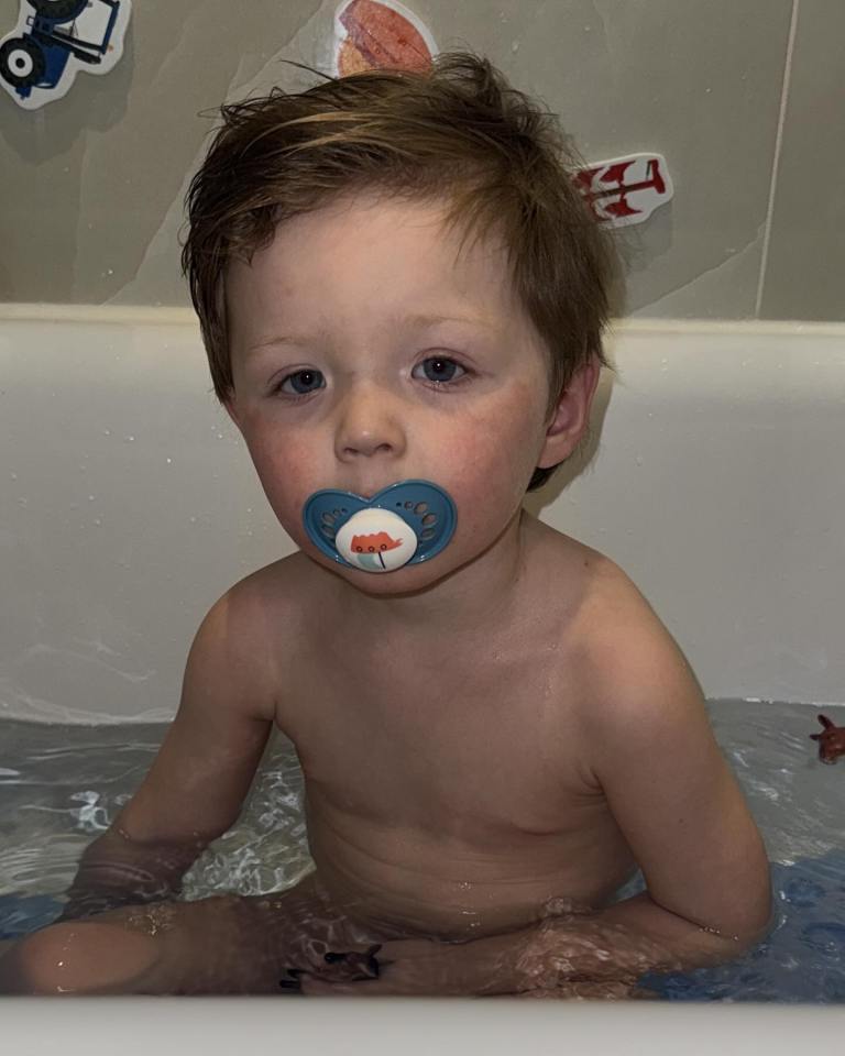 Toddler in a bath with a pacifier.