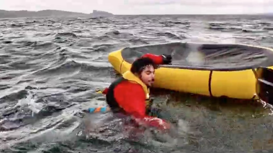 Man clinging to overturned packraft in choppy water.