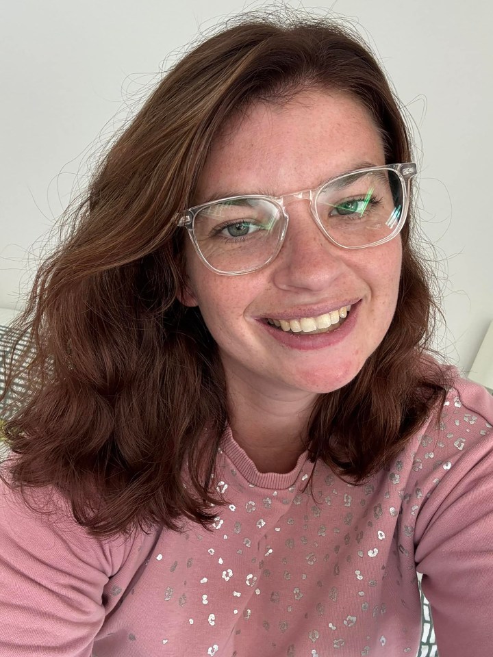 Close-up selfie of a woman wearing clear glasses and a pink sweatshirt.