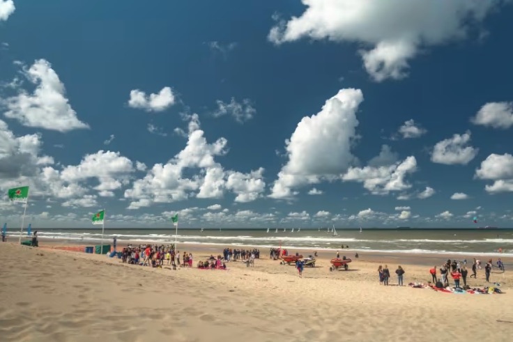 Beach scene with people and sailboats under a cloudy sky.