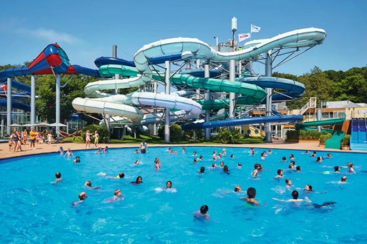 People swimming in a large pool with water slides in the background.