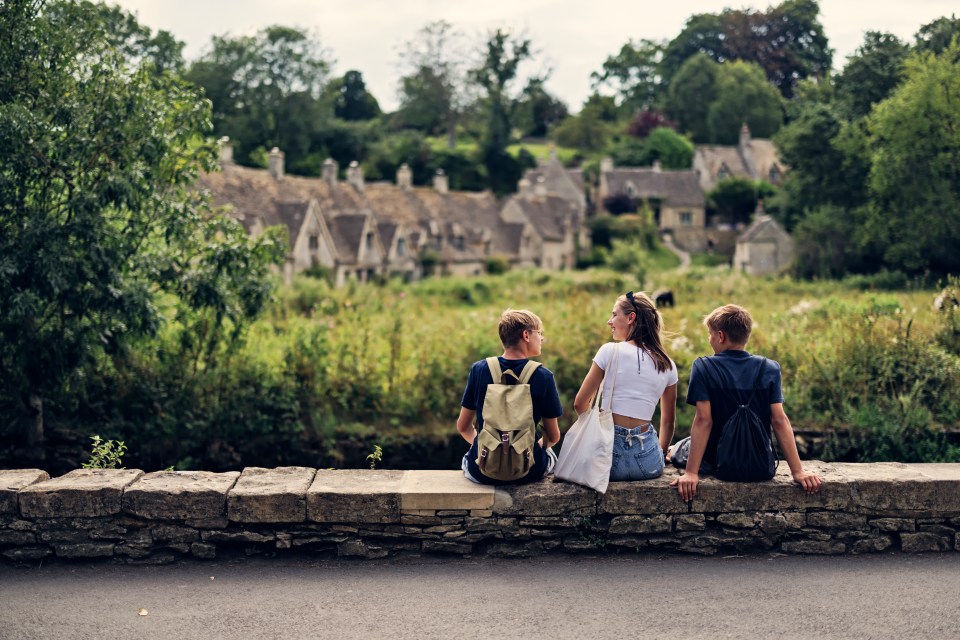 Three teenagers sitting on a low stone wall, looking at a village in the distance.