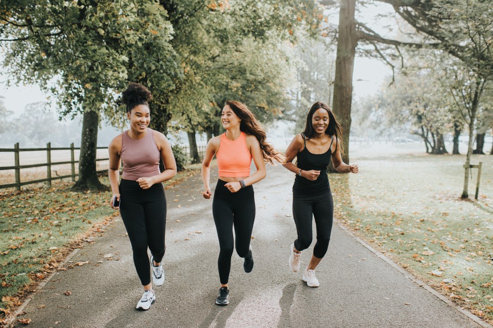 Strong, fit woman joggers, running through a sunny park. They chat and laugh as they exercise with each other. Their hair blows behind them as they look in front of them. They run towards the camera. Space for copy.