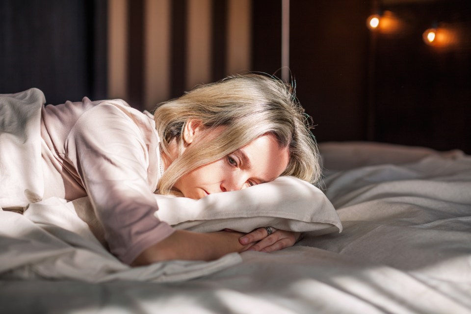 A middle-aged woman lying in bed looking sad.