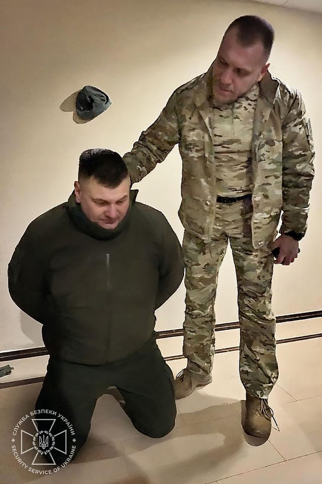 A man in handcuffs kneeling before a uniformed officer.