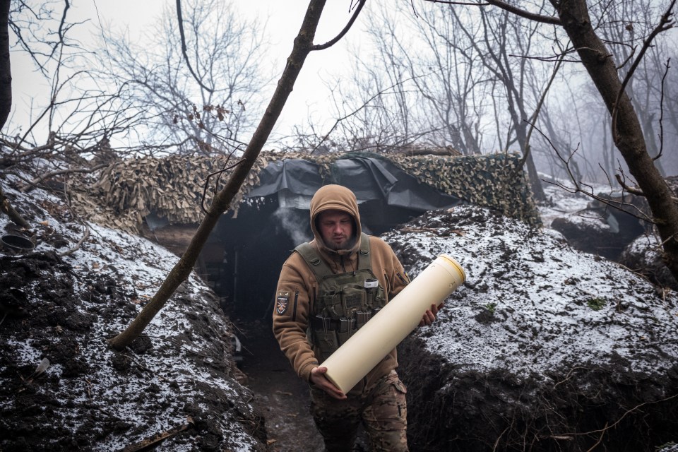 Ukrainian artilleryman carrying a large shell in a snowy forest.