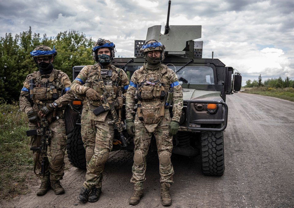 Three Ukrainian servicemen posing with rifles near a military vehicle.