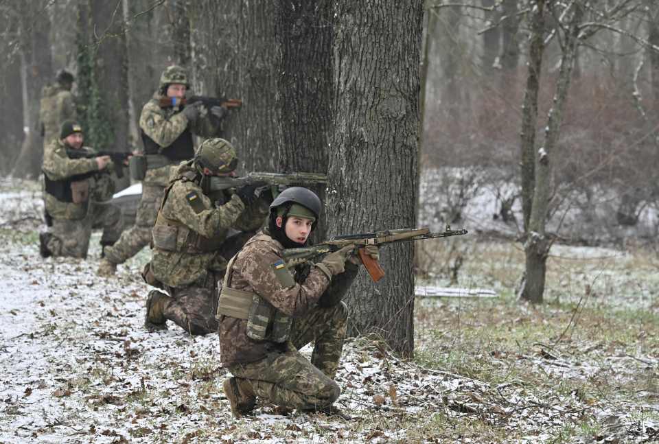 Ukrainian soldiers in camouflage taking firing positions during a military training exercise.