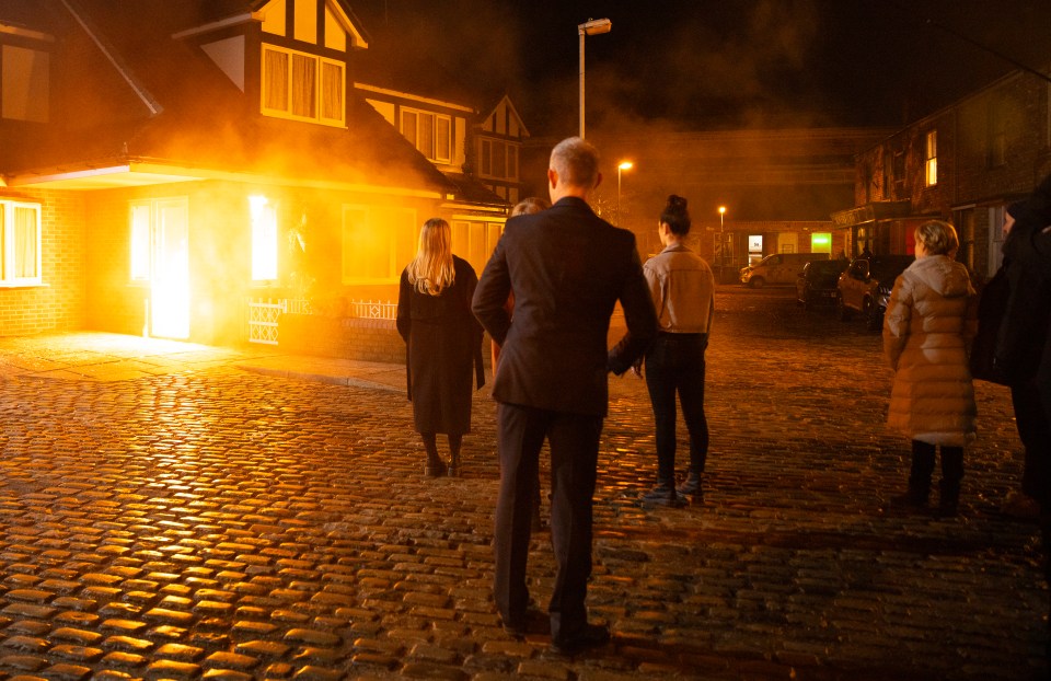 A house fire; several people watch from a cobblestone street.