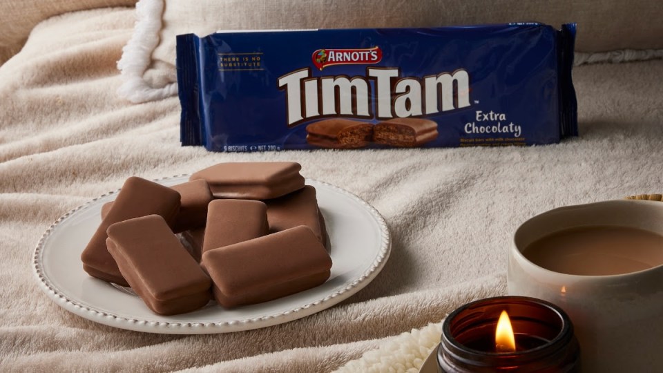 Tim Tam biscuits on a plate with a cup of tea and a candle.