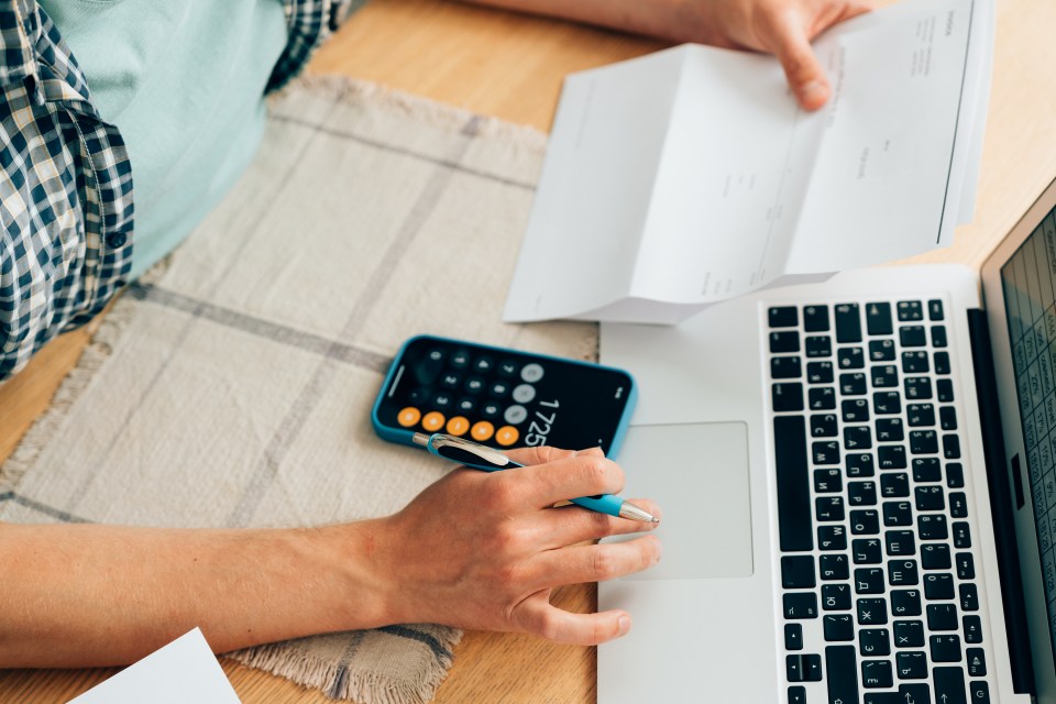 Person reviewing bills and using a calculator and laptop.