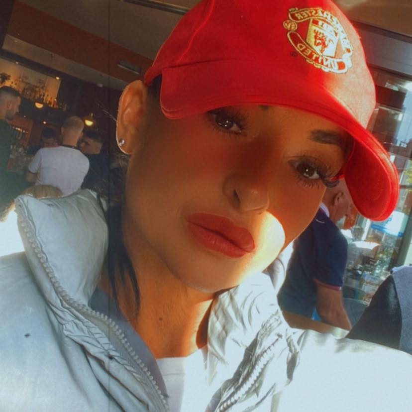 Close-up selfie of a woman wearing a Manchester United baseball cap.