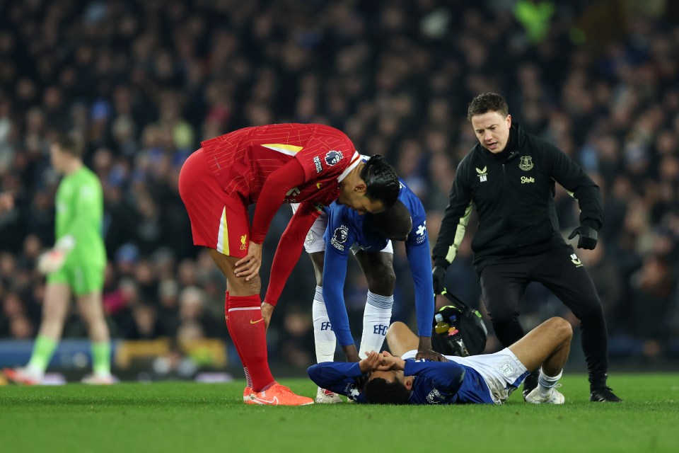 Liverpool and Everton players attending to an injured player on the field.