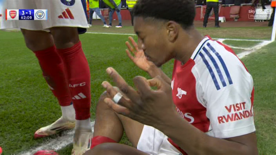 Soccer player sitting on the field looking at his injured hand.