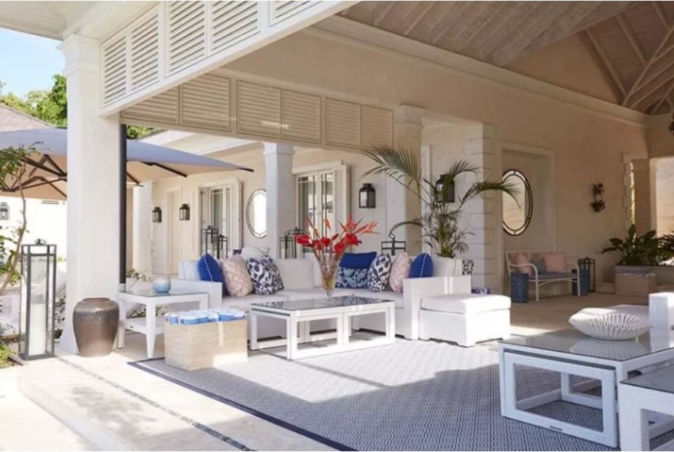 Luxury villa patio with white furniture and blue patterned rug.