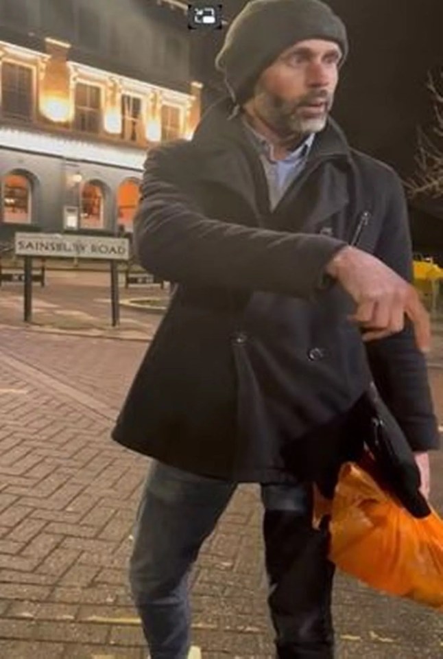 Man in a coat holding an orange bag at night.