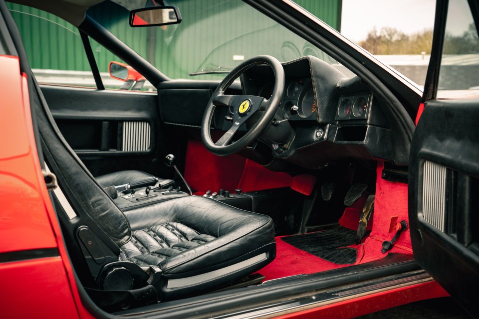 Interior of a red 1977 Ferrari 512 BB Wide Body with black leather seats and red carpeting.