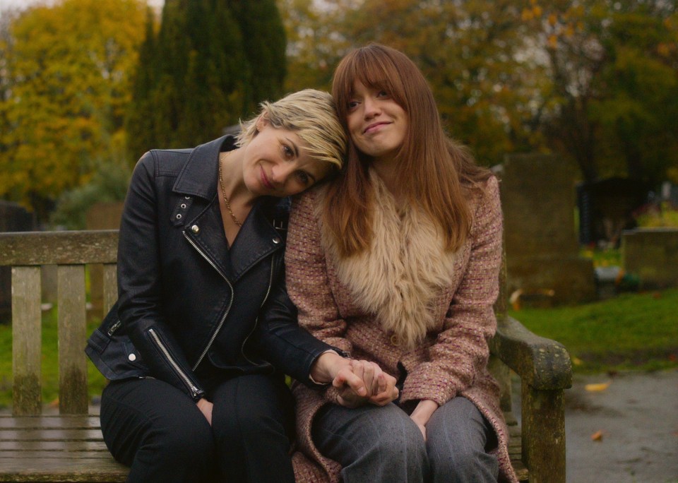 Two women holding hands and sitting on a park bench.