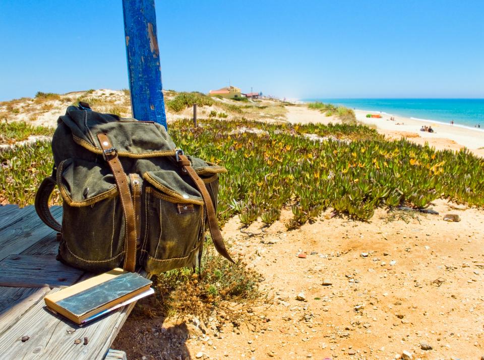 E6Y2D1 Backpack and book on the porch of a wooden hut next to the shore of a European beach. Backpacking traveller taking a break in a