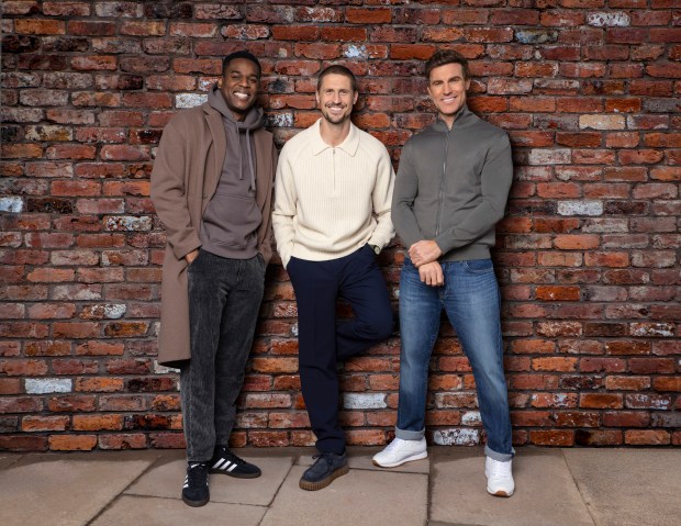 Three men standing against a brick wall.