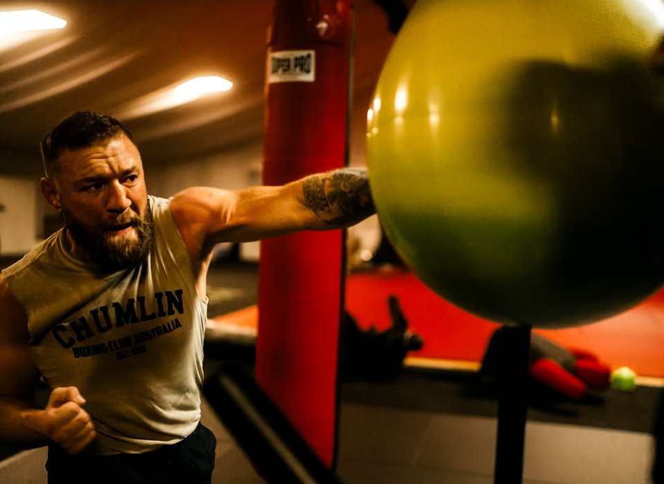 Man punching a large exercise ball during boxing training.