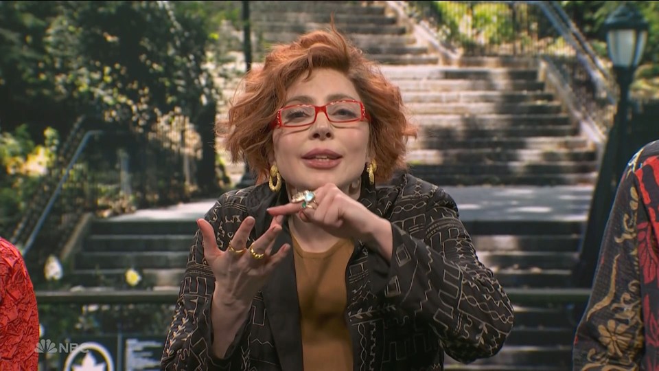 A woman with red hair and glasses speaks, gesturing with her hands.