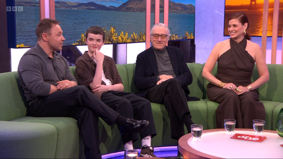 Screenshot of four people sitting on a green couch.