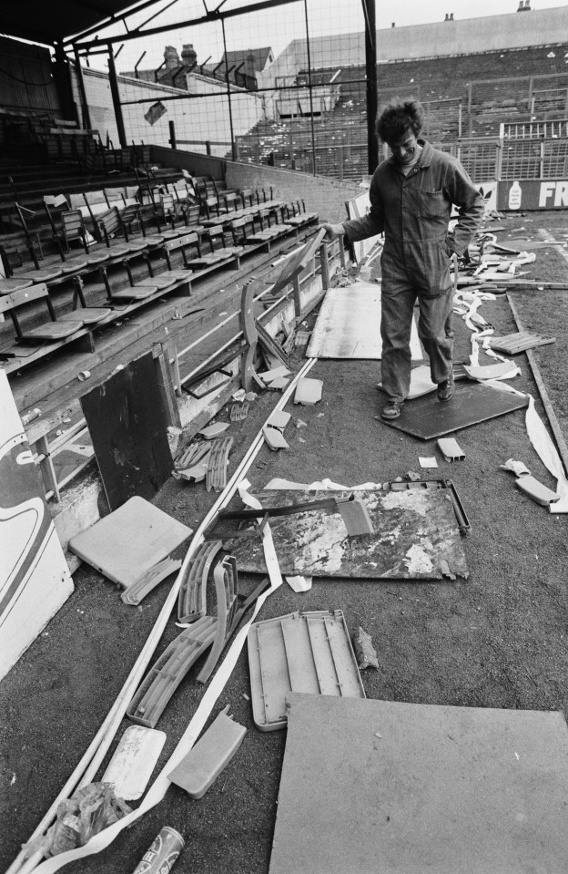 A man cleans up broken stadium seating after a riot.