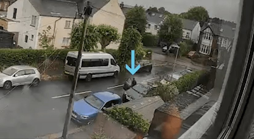 Security camera footage of a person near several cars on a residential street.