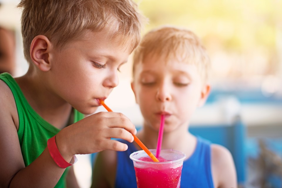 Two young boys sharing a slushy drink with straws.