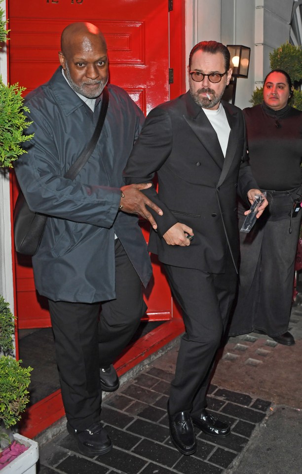 Danny Dyer leaving a party in London, escorted by a security guard.