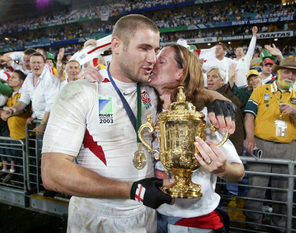 Ben Cohen kissing his wife while holding the Rugby World Cup trophy.