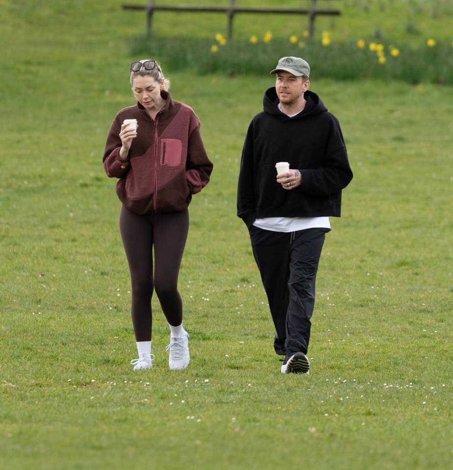 Danny and Georgia Jones walking in a park, holding coffees.