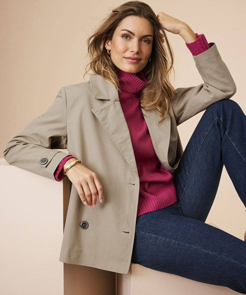 Woman in beige jacket, fuchsia turtleneck, and jeans.