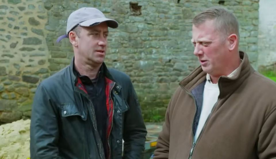 Two men talking in front of a stone wall.